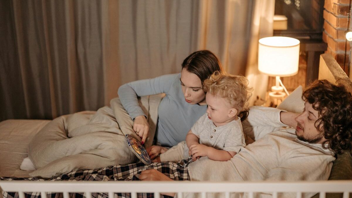 Rodiče s malým dítětem večer leží v posteli a hrají si.