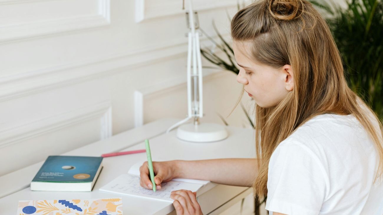 Dívka sedí u stolu a píše domácí úkoly.