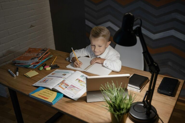 Chlapec sedí u stolu osvětleného stolní lampou a píše domácí úkoly.