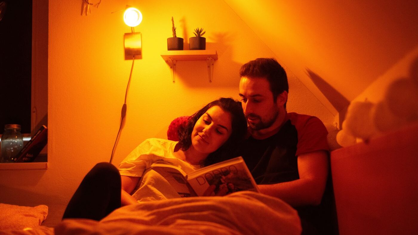 Mladý pár si večer čte a svítí večerní žárovka Oranžovka.