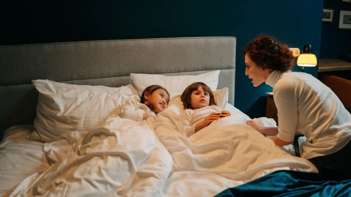 Maminka si večer povídá se dvěmi dětmi, které leží v posteli.