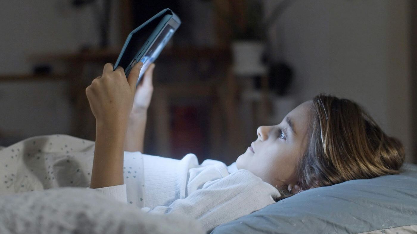 Dívka leží v posteli a sleduje tablet.