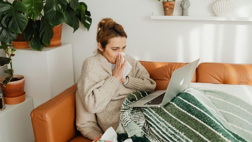 Nemocná žena sedí na gauči a pracuje na počítači