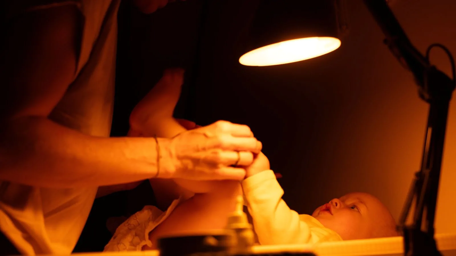 Žena přebaluje dítě a u toho jí svítí večerní žárovka Oranžovka