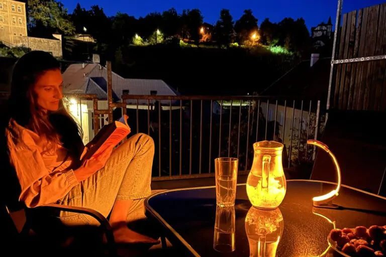 Žena si čte na terase a svítí jí lampička Oranžovka
