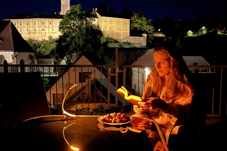 Žena si čte na terase a svítí jí lampička Oranžovka