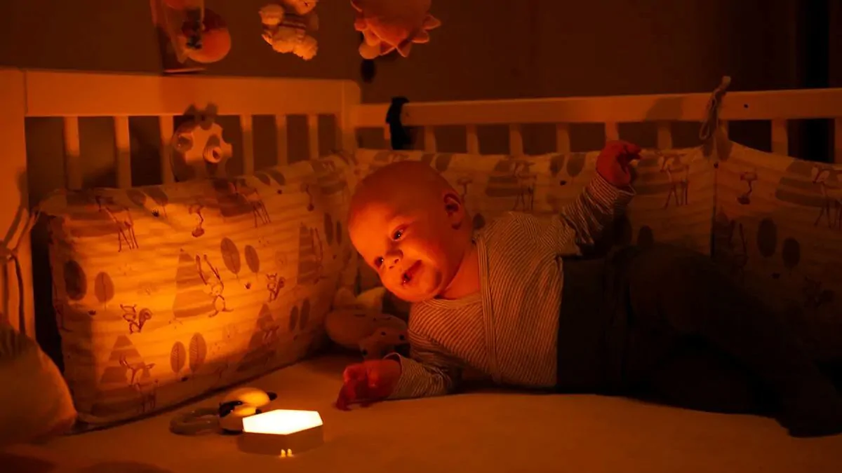 Miminko leží v postýlce a sleduje noční světlo Oranžovka