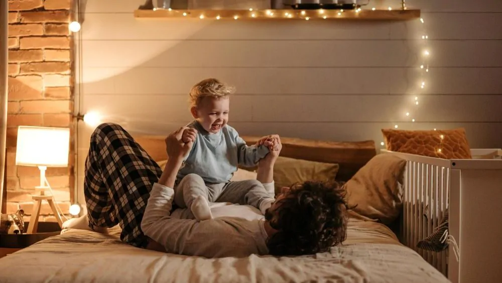 Otec s dítětem leží na posteli a hrají si