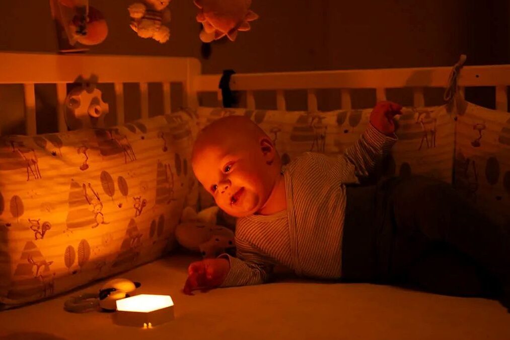 Miminko leží v postýlce a sleduje noční světlo Oranžovka